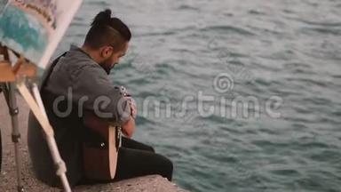 年轻的天才夫妇坐在海边，做着业余爱好。 女人画画，男人弹吉他。
